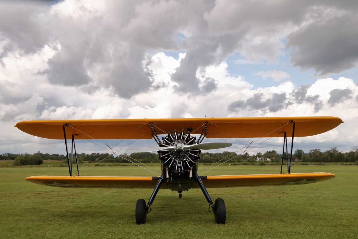 Front view of a yellow biplane under a cloudy sky