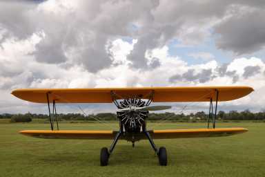 Front view of a yellow biplane under a cloudy sky