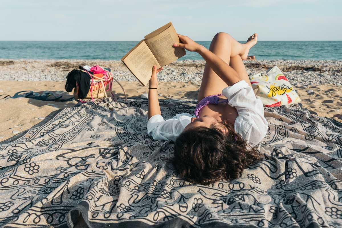Young woman relaxing on beach towel reading book at the beach
