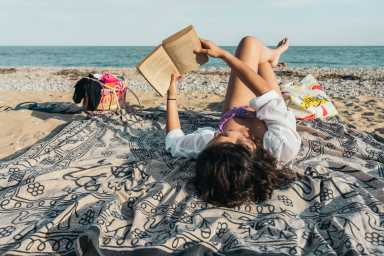 Young woman relaxing on beach towel reading book at the beach