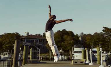 The Fire Island Dance Festival, returning July 18-19 to Fire Island Pines, is set on a waterfront stage overlooking the Great South Bay. The festival gathers extraordinary dancers in a place where salt air, open sky, and communal memory become part of the performance. Here, dance is not merely entertainment. It is witness, offering, and love made visible, moving from the stage into real life through meals, medication, counseling, emergency assistance, testing, grants, and care.